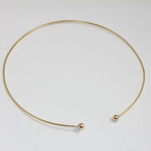 May include: A gold choker necklace with two small round balls at the ends.