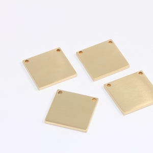 Könnte beinhalten: Vier quadratische Metalletiketten in Goldfarbe mit jeweils zwei Löchern. Die Etiketten sind leer und bereit zur Personalisierung.