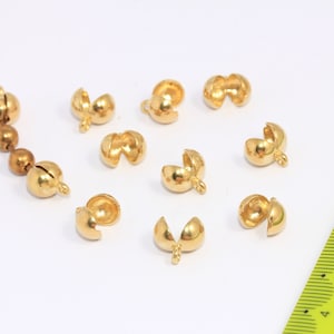 May include: A close-up of ten gold-colored metal bead caps. The caps are designed to be used as end caps for necklaces or bracelets. The caps are open on one side and have a small loop on the other side.
