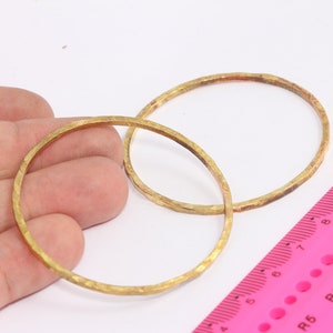 Op de afbeelding: Twee gouden metalen hoepels, waarvan er één iets groter is dan de andere, liggen op een hand. Een roze liniaal met zwarte markeringen is op de achtergrond te zien.