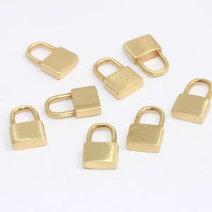 May include: Eight gold-toned padlock charms with a square shape. The charms have a small loop at the top for attaching to a necklace, bracelet, or other jewelry.