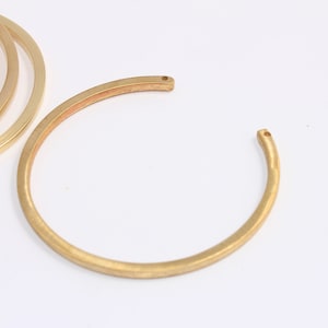Könnte beinhalten: Vier goldfarbene Metallarmbänder, die übereinander gestapelt sind. Ein fünftes Armband liegt flach auf der Oberfläche.