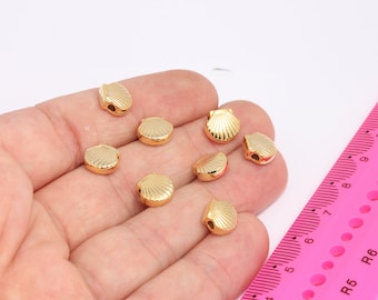 May include: A close-up of a hand holding eight gold-colored seashell-shaped beads. The beads are about 1 cm in diameter and have a smooth, shiny finish.