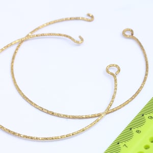 May include: Two gold-toned hoops with textured surfaces. The hoops are approximately 15 cm in diameter and have a small loop at the top for attaching to earrings.