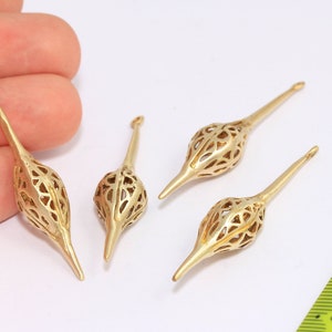 Może przedstawiać: Cztery złote metalowe wisiorek w kształcie łzy z ostrym końcem. Wisiorek mają około 5 cm długości i mają delikatny, misterny wzór.