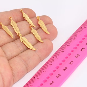 Op de afbeelding: Zes gouden verencharms met een lus aan de bovenkant om te bevestigen aan sieraden of andere knutselwerkjes.