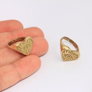 Könnte beinhalten: Zwei goldfarbene Ringe mit einem herzförmigen Design, das ein Augenmotiv zeigt. Die Ringe sind verstellbar und können an jedem Finger getragen werden.