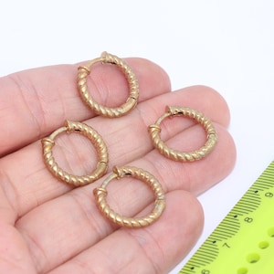 Puede incluir: Cuatro pendientes de aro dorados con un diseño de cuerda trenzada. Los pendientes tienen un diámetro de aproximadamente 2,5 cm.