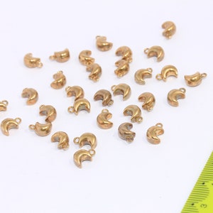 May include: A collection of 20 gold-toned metal crescent moon charms with a loop at the top for attaching to jewelry or other crafts.