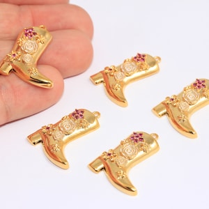 May include: Five gold-tone metal charms shaped like cowboy boots with pink and white floral details. Each charm has a loop for attaching to a necklace or bracelet.