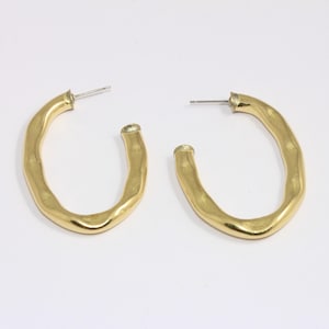 May include: A pair of gold-toned hoop earrings with an irregular, slightly oval shape. The earrings have a hammered texture and a smooth finish.