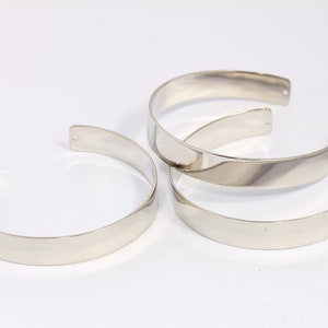 Könnte beinhalten: Drei silberne Metallarmbänder, jedes mit einer glatten, flachen Oberfläche und einer leicht abgerundeten Kante.