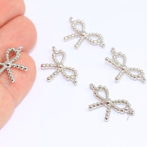 Op de afbeelding: Vijf zilveren bedels in de vorm van een strik met een parelmoerontwerp. De bedels zijn klein en delicaat en perfect om een ​​toets van elegantie toe te voegen aan sieraden of knutselwerk.
