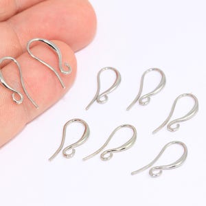 Puede incluir: Un conjunto de diez ganchos para pendientes de color plateado. Los ganchos están hechos de metal y tienen un acabado liso y pulido.