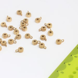 May include: A group of 20 gold-coloured metal bead caps with a small loop on the top. The bead caps are scattered on a white surface.