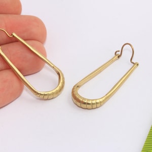 Può includere: Un paio di orecchini a cerchio dorati con un design testurizzato e rigato. Gli orecchini sono lunghi circa 5 cm.