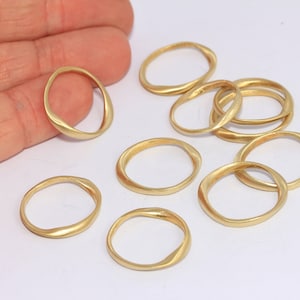 Könnte beinhalten: Ein Satz von zehn goldfarbenen Ringen, jeder mit einer leicht unregelmäßigen, wellenförmigen Form. Die Ringe liegen lose auf einer weißen Oberfläche.