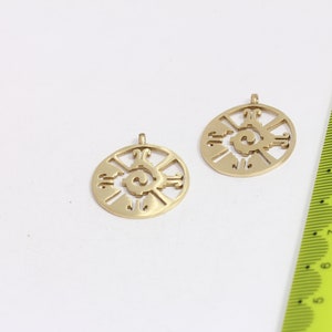 May include: Two gold-colored metal pendants with a circular design featuring a stylized sun symbol. The pendants are approximately 2 cm in diameter.