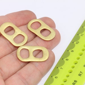 May include: Three gold-colored metal rings with two holes each. The rings are lying on a hand, with a ruler in the background.