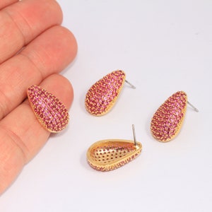 May include: A pair of gold teardrop earrings with pink cubic zirconia stones.