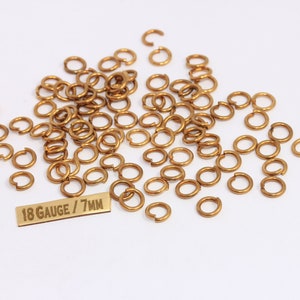 May include: A pile of gold jump rings, 18 gauge and 7mm in diameter, on a white background. The jump rings are used for jewelry making.