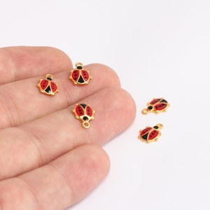 Puede incluir: Cinco abalorios de mariquita de color dorado con esmalte rojo y negro. Los abalorios tienen un bucle en la parte superior para sujetarlos a joyas u otras manualidades.