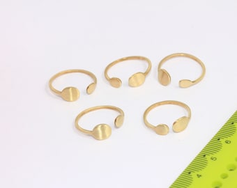 Puede incluir: Cinco anillos de oro con un corte circular en cada anillo. Los anillos están dispuestos en un semicírculo sobre una superficie blanca.