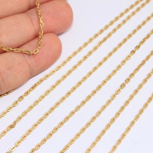 Può includere: Più fili di catena dorata, probabilmente per la creazione di gioielli, sono disposti su una superficie bianca. La catena è di stile delicato, con maglie ovali.
