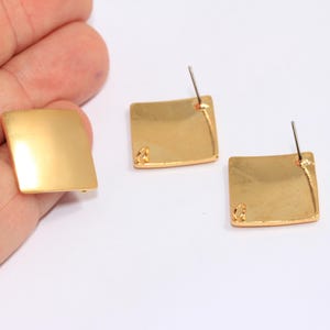 Könnte beinhalten: Ein Paar goldene quadratische Ohrringe mit gebürsteter Oberfläche. Die Ohrringe haben einen Stiftverschluss.