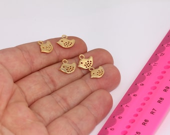 May include: Five gold-colored metal charms shaped like birds with a hole at the top for attaching to a chain or bracelet. The charms are on a hand against a pink ruler.