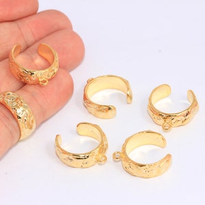 Puede incluir: Cinco anillos de metal dorado con una superficie texturizada. Los anillos tienen un diseño ligeramente abierto y un pequeño bucle en un lado.