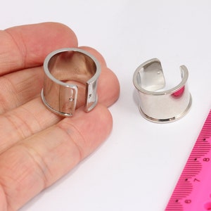 May include: Two silver adjustable rings, one is open and the other is closed, on a hand against a white background with a pink ruler.