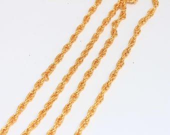 May include: Close-up of multiple strands of gold-colored rope chain. The chains are arranged diagonally against a white background. The chains have a twisted rope design, and the gold color is bright and shiny.