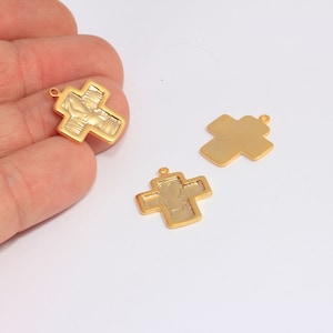 Puede incluir: Tres dijes de cruz de metal de color dorado. Dos de las cruces tienen una superficie texturizada, y una es lisa.