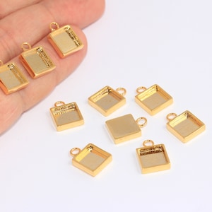May include: Nine gold-tone metal square pendant trays with a loop for hanging. The trays are empty and ready for resin or other embellishments.