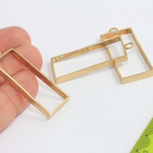 Può includere: Tre cornici rettangolari in metallo dorato con un anello in cima per appenderle. Le cornici sono di dimensioni diverse e sono disposte su una superficie bianca.