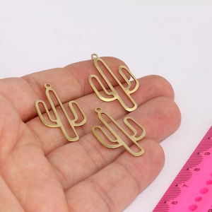 Op de afbeelding: Drie gouden metalen cactusbedels met een uitgesneden ontwerp. De bedels zijn ongeveer 5 cm hoog en hebben een lus aan de bovenkant om aan sieraden of andere knutselwerken te bevestigen.