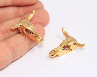 May include: Two gold-tone metal bull skull charms. The charms are detailed with a hollowed-out skull design and horns.