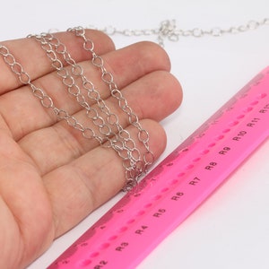 Puede incluir: Un collar de cadena de plata con múltiples hebras, medido contra una regla rosa con marcas en pulgadas.