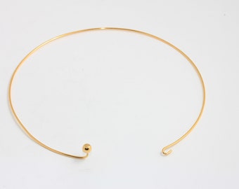 May include: A gold-toned metal choker necklace featuring a thin, circular wire band. One end of the necklace terminates in a small, smooth spherical bead, while the other end features a simple, open hook design for closure and adjustment.