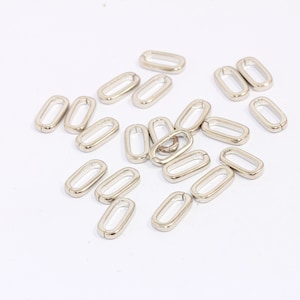 Pode incluir: Um grupo de anéis de metal ovalados prateados. Os anéis medem aproximadamente 2,5 cm de comprimento e 1,25 cm de largura.