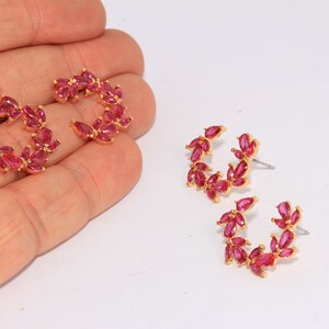 May include: A pair of gold hoop earrings with pink crystal accents. The earrings are shaped like a crescent moon and have a delicate, feminine design.