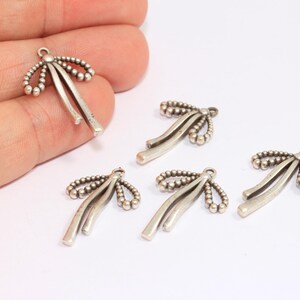 May include: Five silver-toned metal charms shaped like bows with a beaded design.