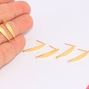 Puede incluir: Cinco hallazgos de pendientes de color dorado con un diseño curvo, plano y en forma de hoja. Los hallazgos tienen un pequeño bucle en la parte inferior y un poste en la parte superior.