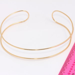 Pode incluir: Um colar choker de duas camadas dourado. O colar é feito de duas faixas finas de metal que são conectadas na parte de trás. O colar tem um diâmetro de aproximadamente 8 polegadas.