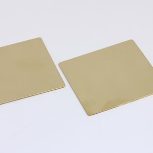 Könnte beinhalten: Zwei quadratische, goldfarbene Metallplatten. Die Platten sind glatt und haben eine leicht reflektierende Oberfläche.