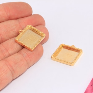 Könnte beinhalten: Zwei quadratische Anhänger-Tabletts in Goldfarbe mit dekorativem Rand. Die Tabletts sind etwa 2,5 cm groß.