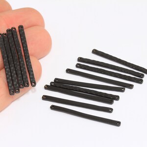 Könnte beinhalten: Ein Satz mit 15 schwarzen Metall-Stangenverbindern mit gehämmerter Textur und zwei Löchern an jedem Ende. Die Verbinder sind etwa 3,8 cm lang.