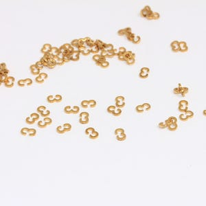 May include: A scattering of gold-colored metal number three charms on a white background.