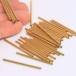May include: A pile of 25 gold brass tubes, approximately 2.5 cm long, with a ruler in the background.